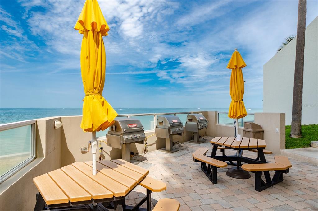 An outdoor patio features two picnic tables with yellow umbrellas and three stainless steel grills — 450 S GULFVIEW BOULEVARD UNIT 405, CLEARWATER, FL
