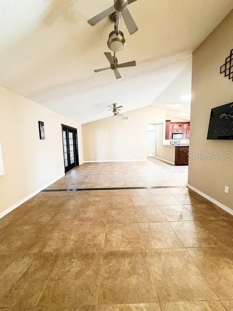 A spacious room features light-colored tile flooring, vaulted ceilings with two fans, and a kitchen — 9319 WOODBREEZE BOULEVARD, WINDERMERE, FL