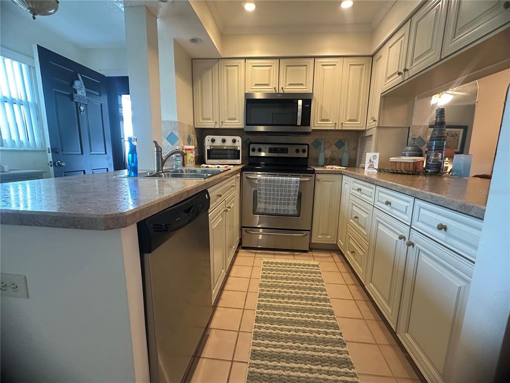 A kitchen features light-colored cabinets, stainless steel appliances, a tiled floor, and a breakfast bar — 202 46TH AVENUE TERRACE W UNIT 409, BRADENTON, FL