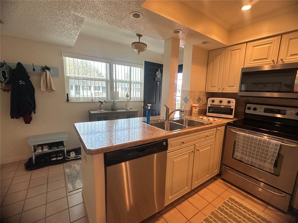A kitchen features stainless steel appliances, light-colored cabinets, a peninsula sink, and tile flooring — 202 46TH AVENUE TERRACE W UNIT 409, BRADENTON, FL