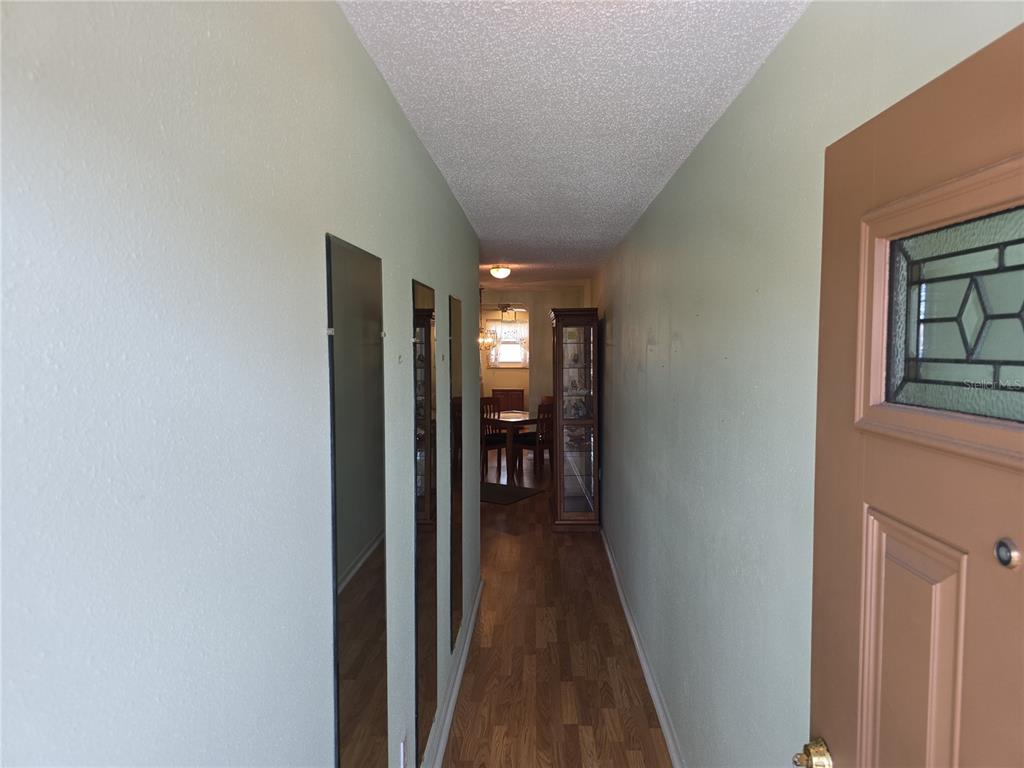 A narrow hallway with light green walls, wood-look flooring, and vertical wall mirrors — 5603 80TH STREET N UNIT 410, ST PETERSBURG, FL