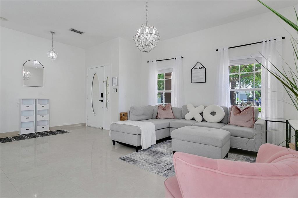 A bright living room features a gray sectional sofa, a pink armchair, and white tile flooring — 4034 FELDSPAR TRAIL, ORLANDO, FL
