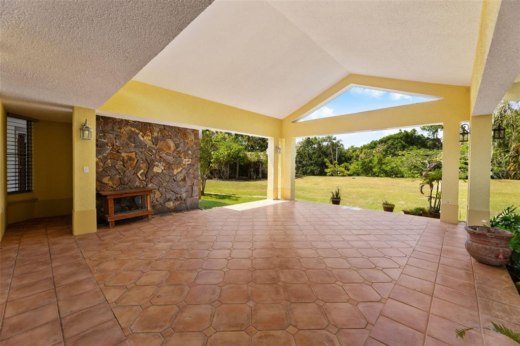 A covered outdoor patio features terracotta tile flooring, a stone accent wall, and vaulted ceilings — 383 CAMINO LOS FLAMBOYANES, CIDRA, PR