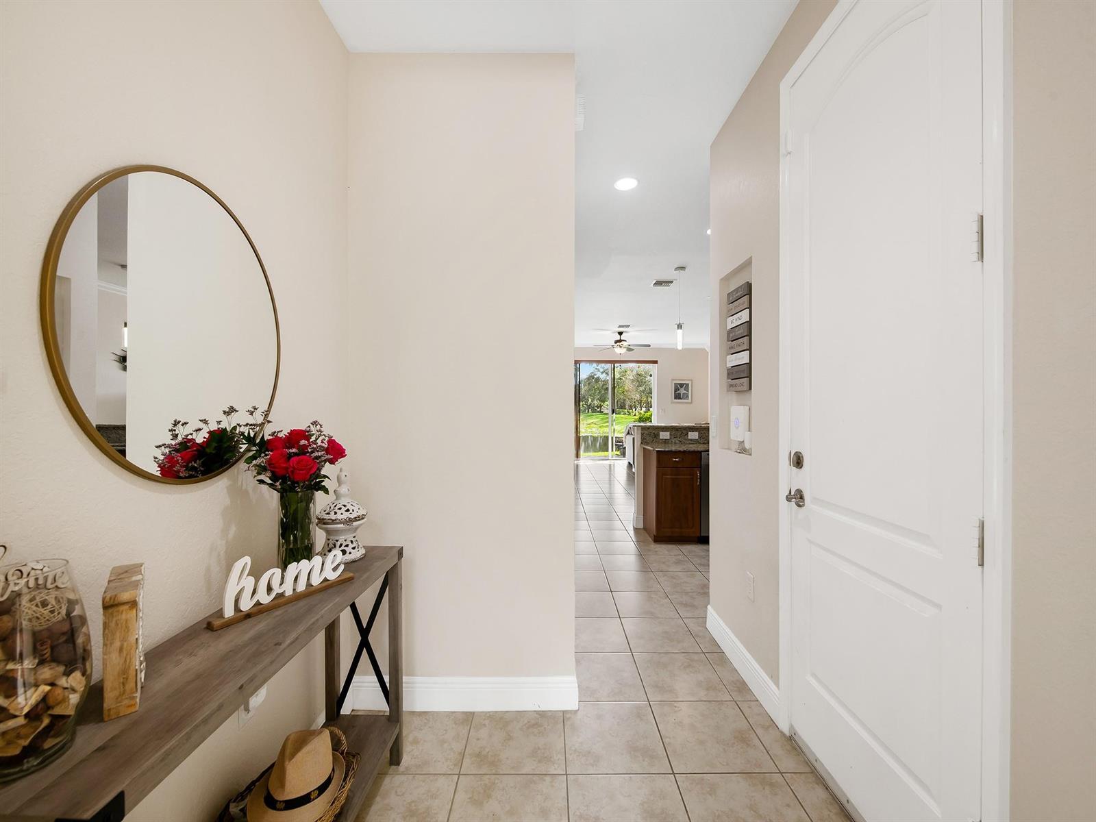 A foyer features a console table, round mirror, and tile flooring leading to an open kitchen — 4792 Sundance Way # 4792, Davie FL 33328, DAVIE, FL