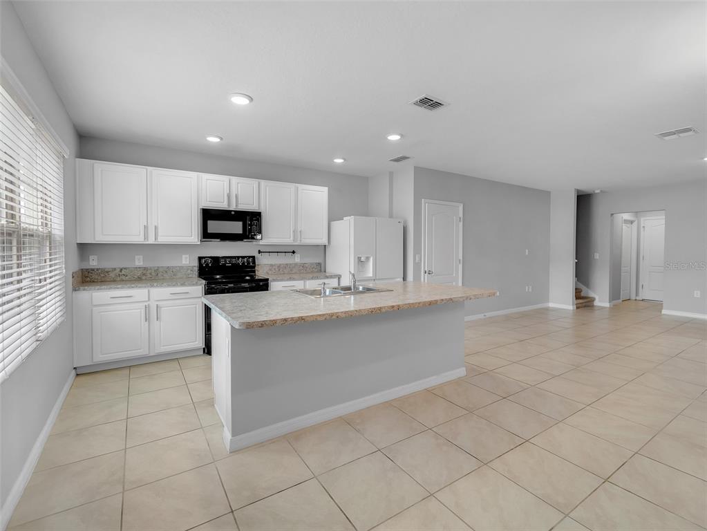 A kitchen features white cabinets, a central island with a countertop, and light tile flooring — 1859 RED CANYON DRIVE, KISSIMMEE, FL