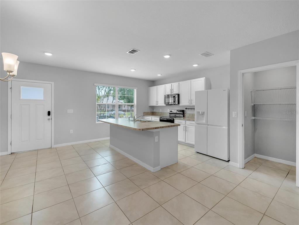 A kitchen with white cabinets, a central island, tile flooring, and an adjacent pantry — 1859 RED CANYON DRIVE, KISSIMMEE, FL