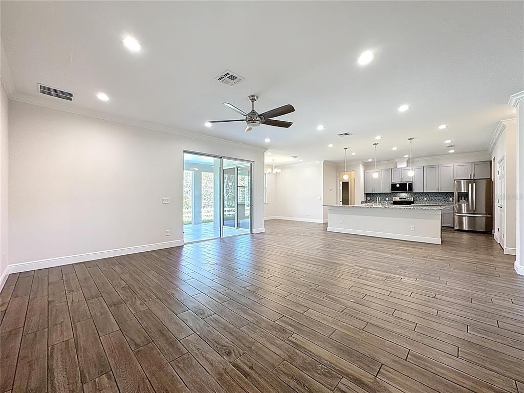 An open-concept living area features wood-look tile flooring, a kitchen island, and sliding glass doors — 3110 CARNEGIE AVENUE, ORLANDO, FL