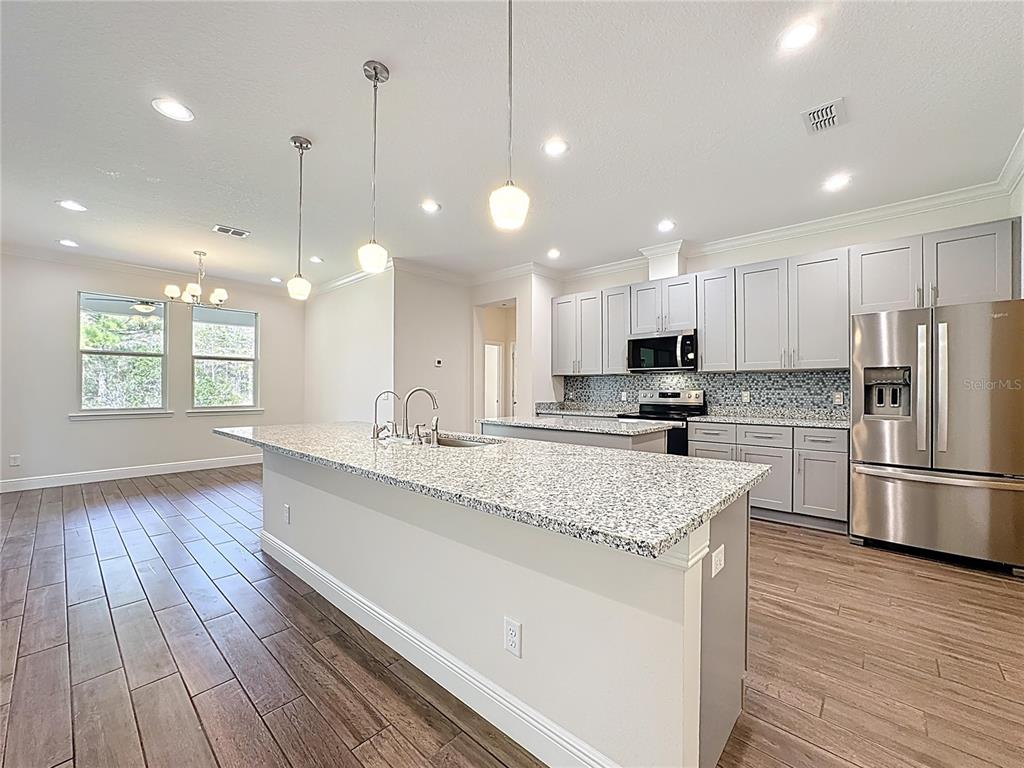 A kitchen features a granite-topped island, light gray cabinets, stainless steel appliances, and wood-look flooring — 3110 CARNEGIE AVENUE, ORLANDO, FL