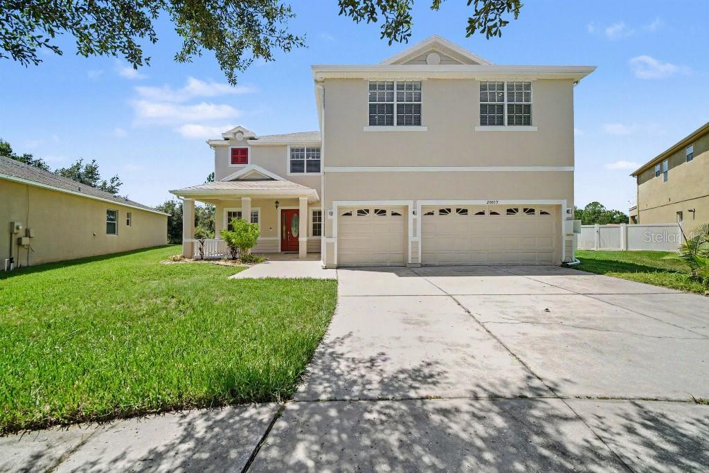 A two-story suburban house with a beige exterior, a two-car garage, and a front porch — 20009 OAKFLOWER AVENUE, TAMPA, FL