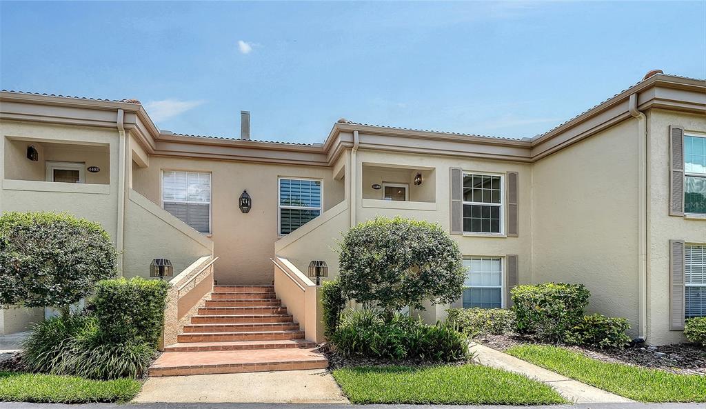 A two-story tan apartment building features a central staircase leading to two recessed entryways — 4489 LONGMEADOW UNIT 74, SARASOTA, FL