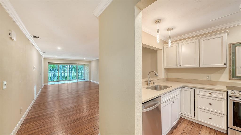 A kitchen with white cabinets and stainless steel appliances opens into a spacious living area — 4489 LONGMEADOW UNIT 74, SARASOTA, FL