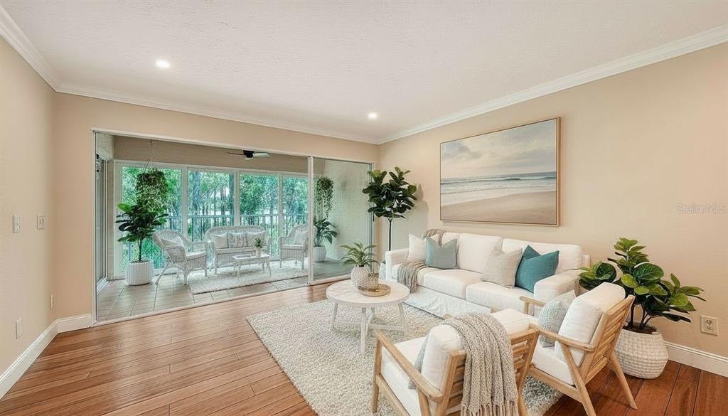 A living room with light wood floors, a white sofa, and sliding doors to a balcony — 4489 LONGMEADOW UNIT 74, SARASOTA, FL
