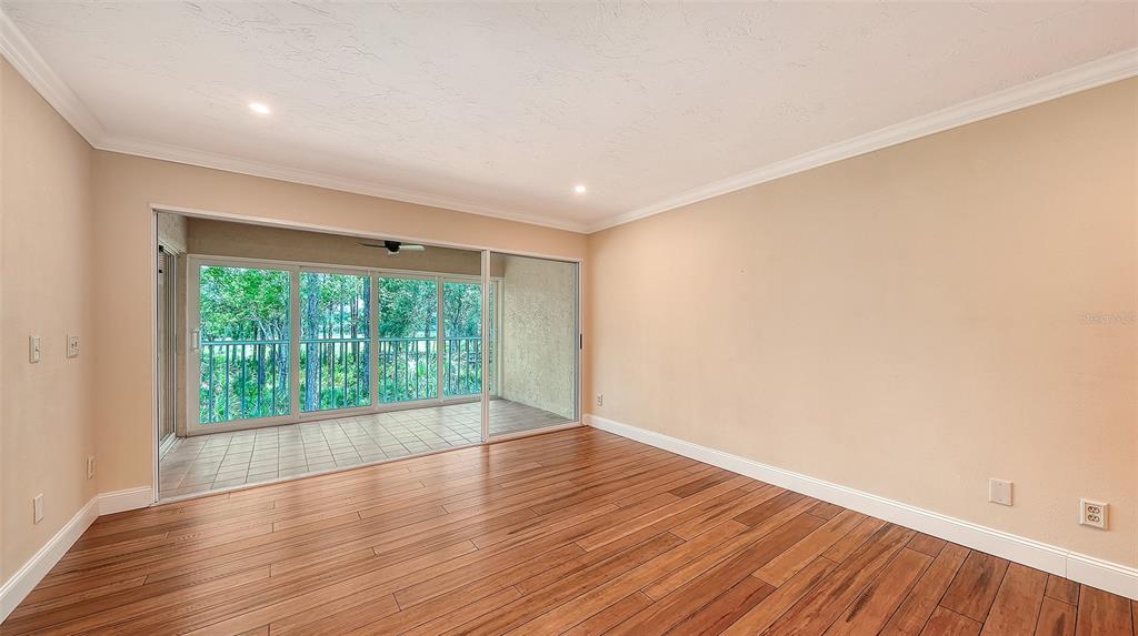 An empty room with wood-look flooring, beige walls, and sliding glass doors to a balcony — 4489 LONGMEADOW UNIT 74, SARASOTA, FL