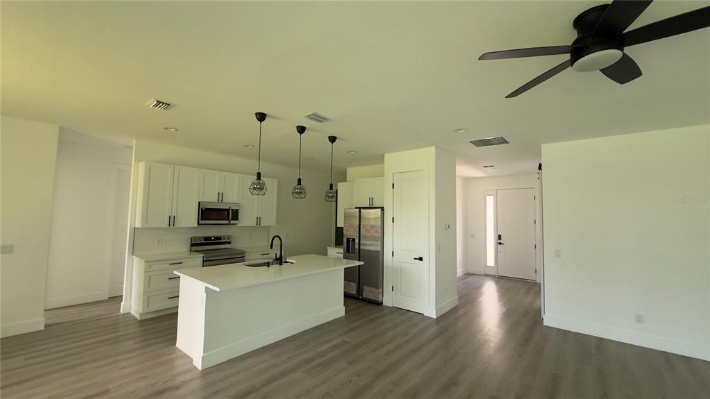 A modern kitchen features white cabinetry, a central island, stainless steel appliances, and wood-look flooring — 14300 SANILAC AVENUE, PORT CHARLOTTE, FL