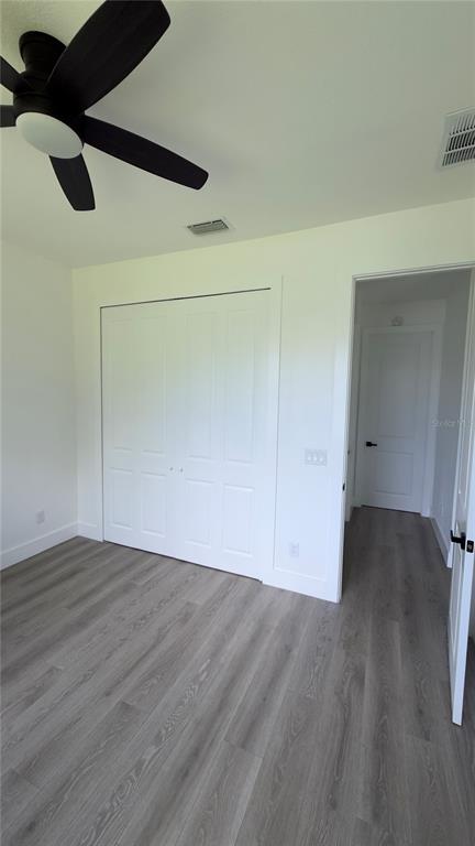 A bedroom with gray wood-look flooring, a ceiling fan, a white closet, and an open doorway — 14300 SANILAC AVENUE, PORT CHARLOTTE, FL