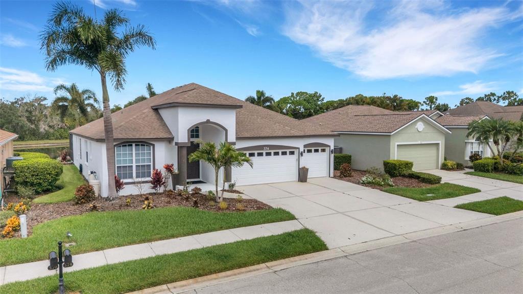 An aerial view shows three suburban houses with driveways and lawns bordering a small pond — 374 LONDONDERRY DRIVE, SARASOTA, FL