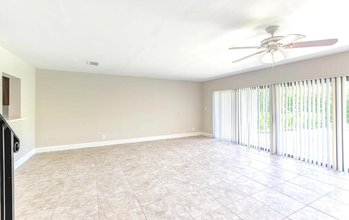 A bright, empty living room features large tile flooring, a ceiling fan, and sliding glass doors — 663 Dover Street # 10, Boca Raton FL 33487, BOCA RATON, FL