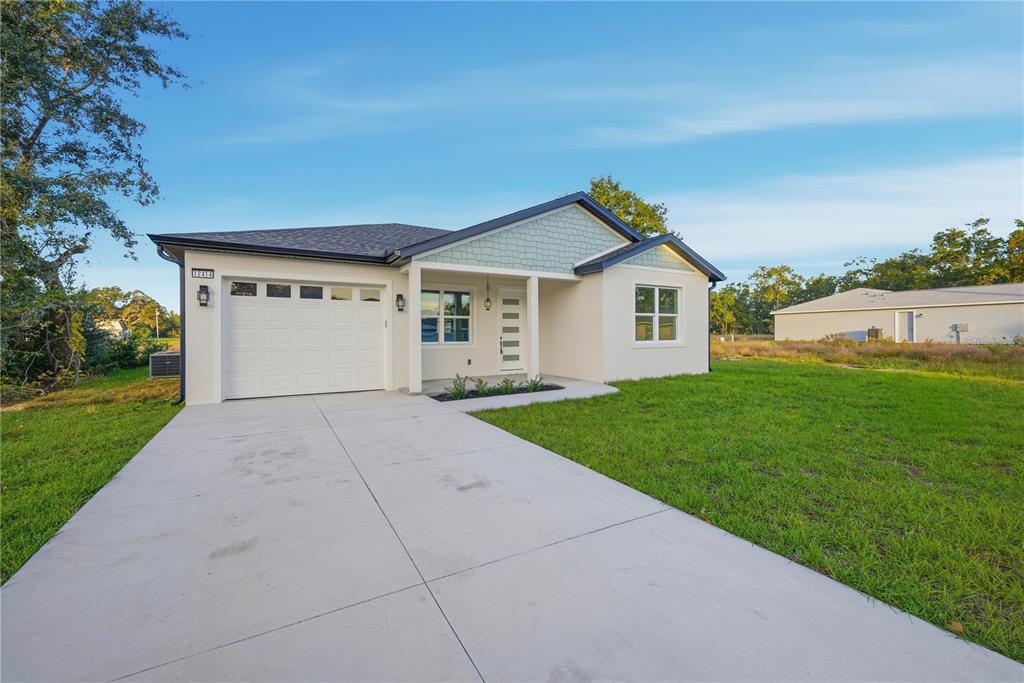 A single-story house with a white garage, light-colored siding, and a concrete driveway — 12414 SE 106TH COURT, BELLEVIEW, FL