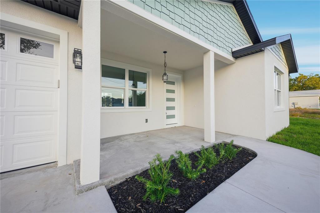 A covered front porch features a white door, a hanging light, and a small garden bed — 12414 SE 106TH COURT, BELLEVIEW, FL