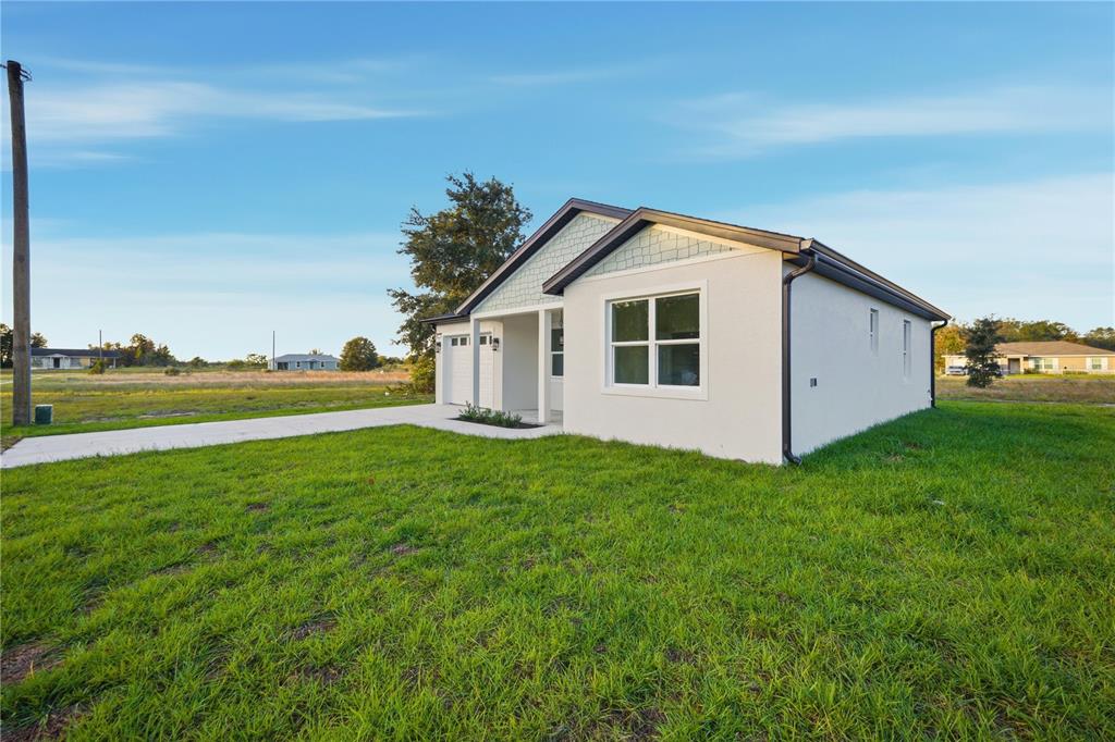 A single-story house with a white stucco exterior and a concrete driveway sits on grass — 12414 SE 106TH COURT, BELLEVIEW, FL