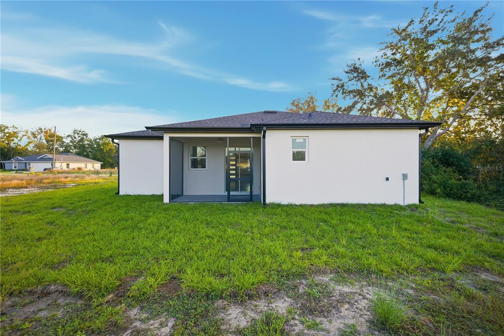 The rear exterior of a single-story house features a screened-in porch and a grassy yard — 12414 SE 106TH COURT, BELLEVIEW, FL