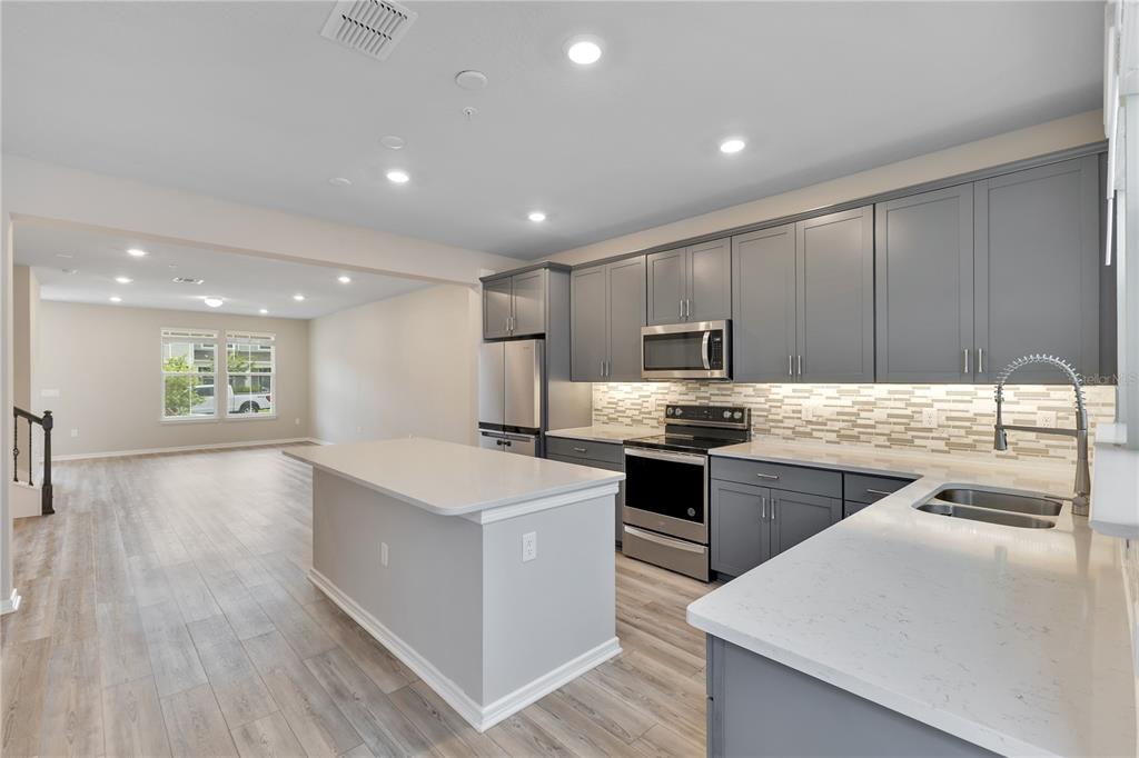 A modern kitchen features gray cabinets, stainless steel appliances, and a white quartz island — 14279 SAPELO BEACH DRIVE, ORLANDO, FL