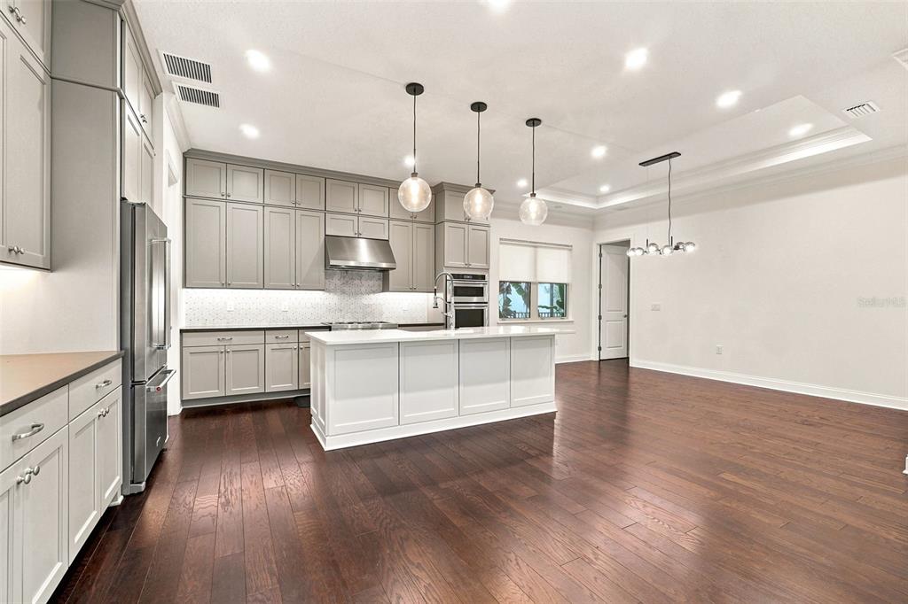 A modern kitchen features gray cabinets, a white island, stainless steel appliances, and hardwood floors — 10134 ROYAL ISLAND COURT, ORLANDO, FL