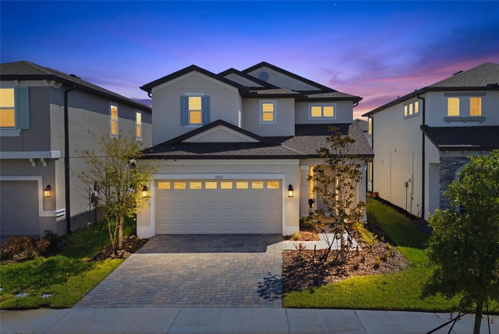 A two-story suburban house with a paved driveway and a two-car garage at dusk — 7273 NOTCHED PINE BEND, WESLEY CHAPEL, FL