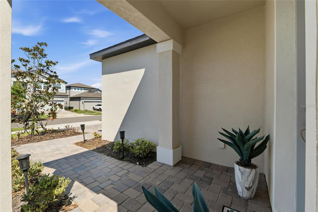A paved entryway features a covered porch, a potted plant, and a view of the street — 7273 NOTCHED PINE BEND, WESLEY CHAPEL, FL