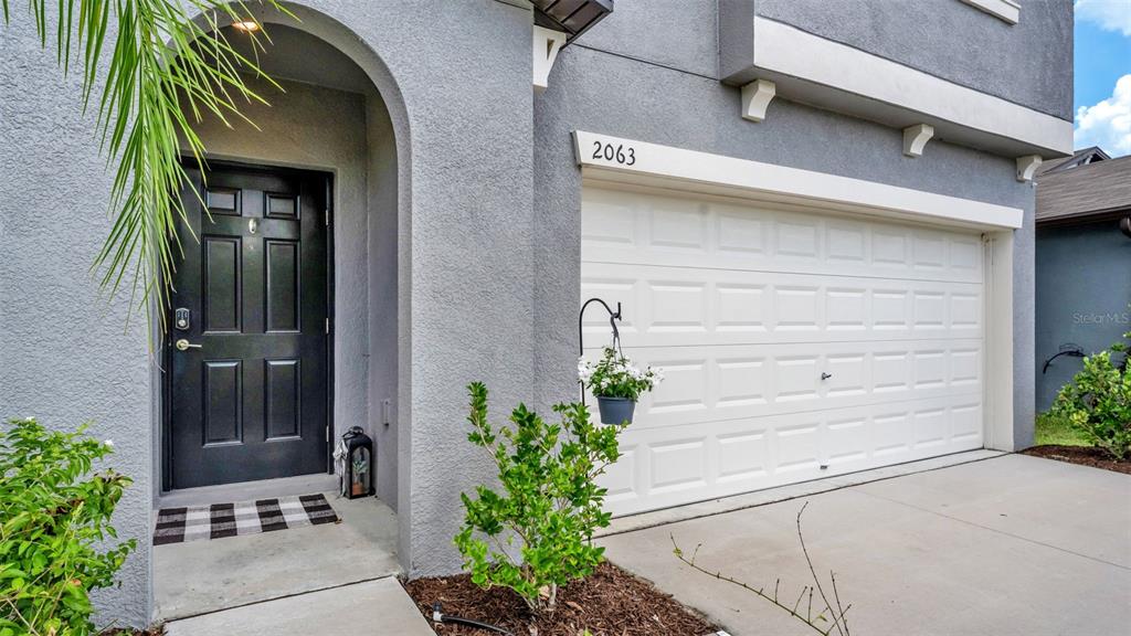 A gray stucco house exterior features a black front door and a white garage door — 2063 OLD PASTURE LANE, LAKELAND, FL