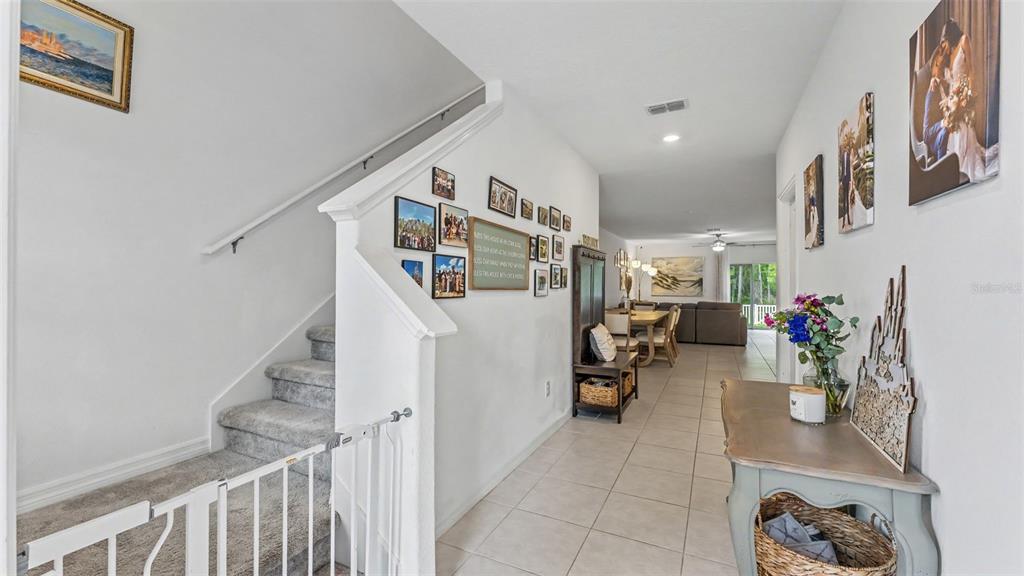 A hallway with a carpeted staircase, tiled floors, and a gallery wall leads to a dining area — 2063 OLD PASTURE LANE, LAKELAND, FL
