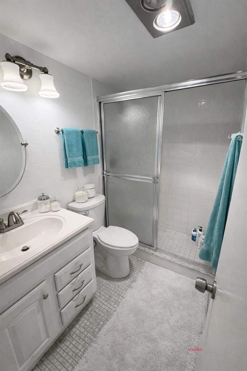 A bathroom features a white vanity, a toilet, and a glass-enclosed shower with white tiles — 7 Lyndhurst A, Deerfield Beach FL 33442, DEERFIELD BEACH, FL