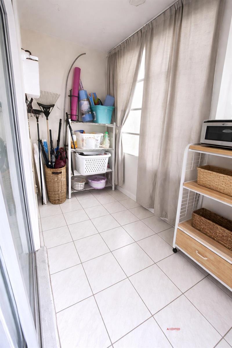 A sunroom with tiled flooring, storage shelving, and a microwave on a rolling cart — 7 Lyndhurst A, Deerfield Beach FL 33442, DEERFIELD BEACH, FL