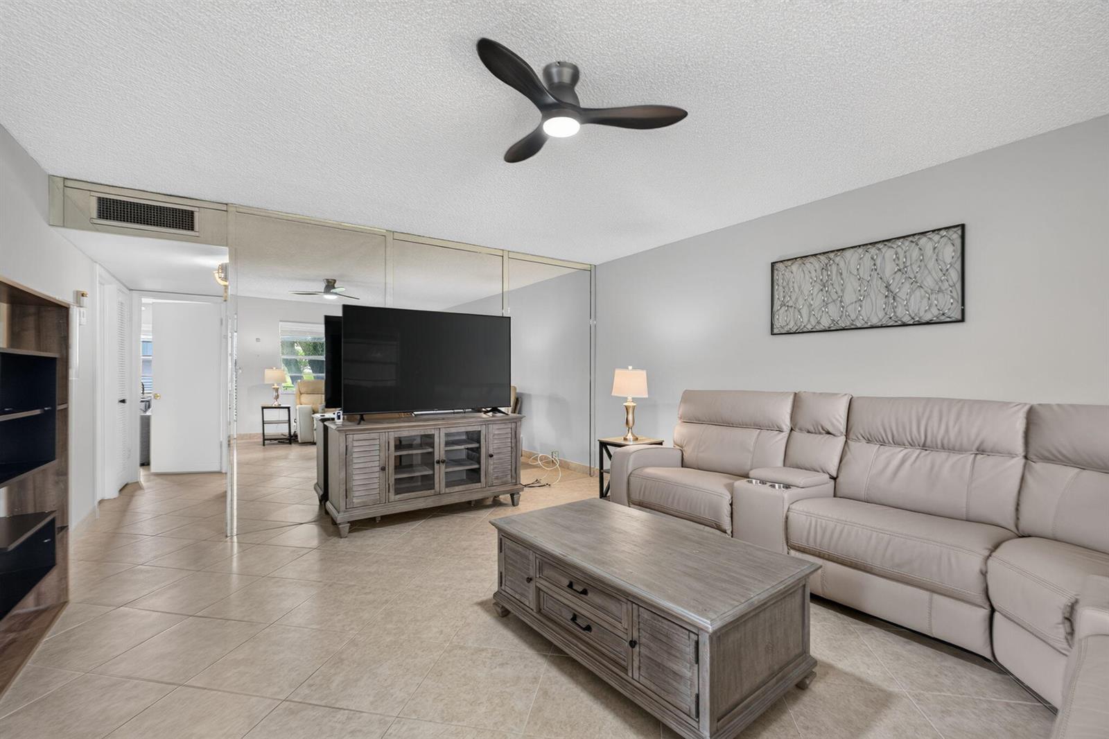 A living room features a beige sectional sofa, a wooden coffee table, and mirrored walls — 942 Normandy T Trail # 942, Delray Beach FL 33484, DELRAY BEACH, FL