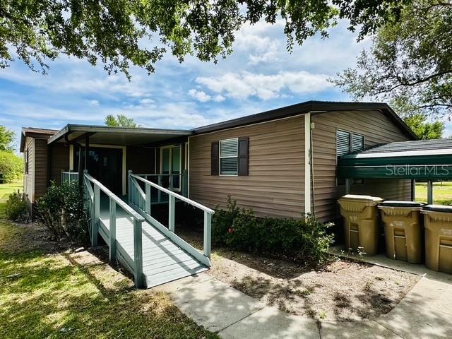 A tan mobile home features a wooden wheelchair ramp leading to a covered entryway — 6814 REDWING ROAD, GROVELAND, FL