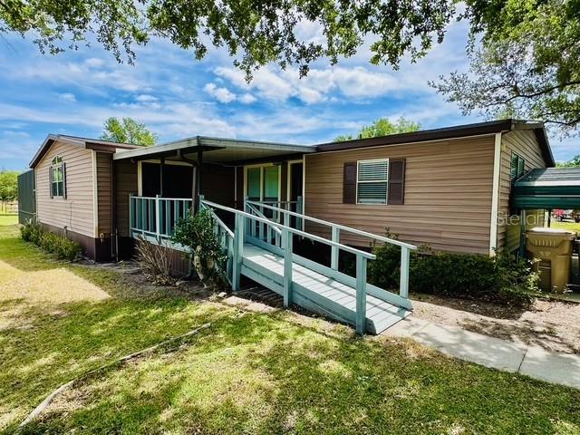 A single-story mobile home with tan siding features a covered porch and a wooden ramp — 6814 REDWING ROAD, GROVELAND, FL