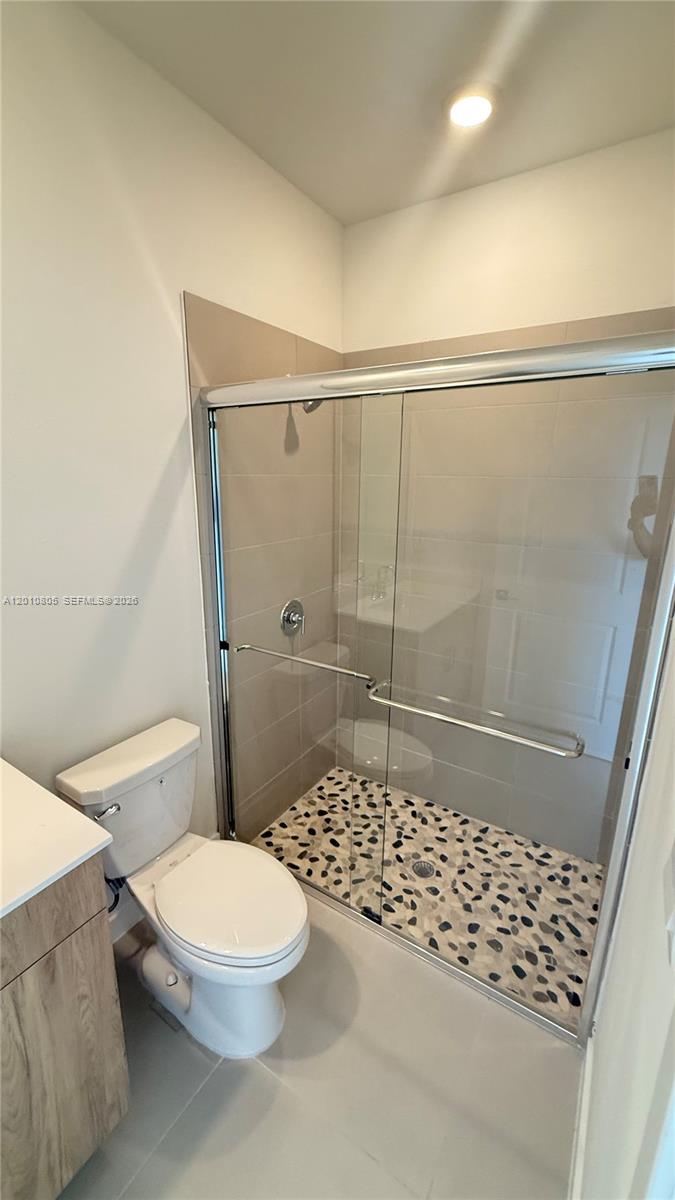 A bathroom features a toilet, a vanity, and a walk-in shower with pebble flooring — 132 NE 13th Cir, Homestead FL 33033, HOMESTEAD, FL