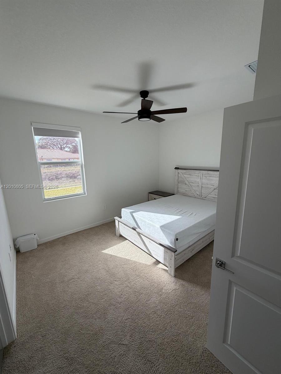 A bedroom features a white bed frame, beige carpet, a ceiling fan, and a window — 132 NE 13th Cir, Homestead FL 33033, HOMESTEAD, FL