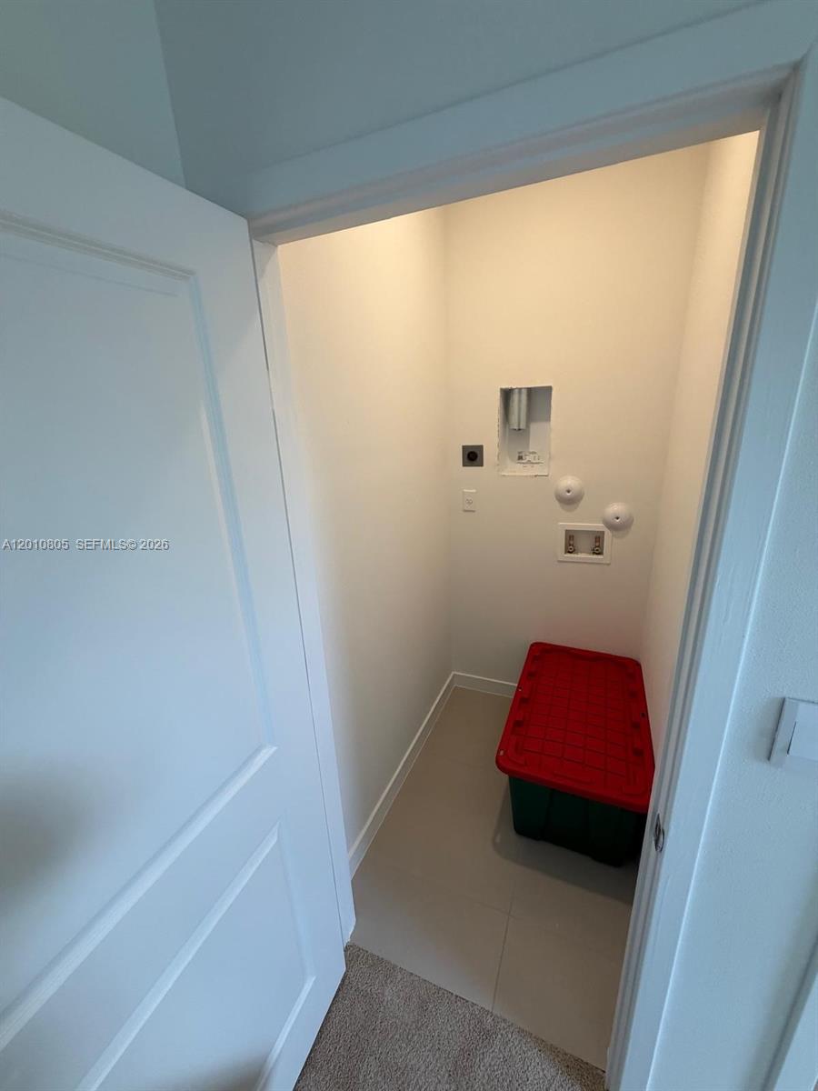 This laundry closet features tile flooring, a red storage bin, and wall-mounted utility hookups — 132 NE 13th Cir, Homestead FL 33033, HOMESTEAD, FL