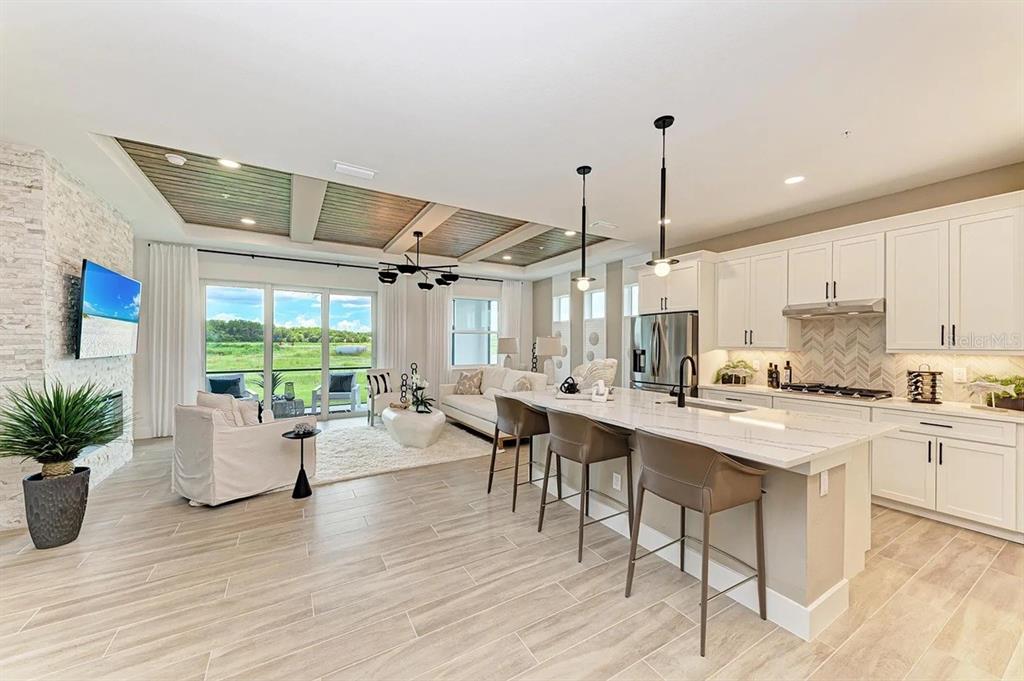 A modern open-concept kitchen and living area with a coffered ceiling and stone fireplace — 10016 REMBRANDT WAY UNIT 101, BRADENTON, FL
