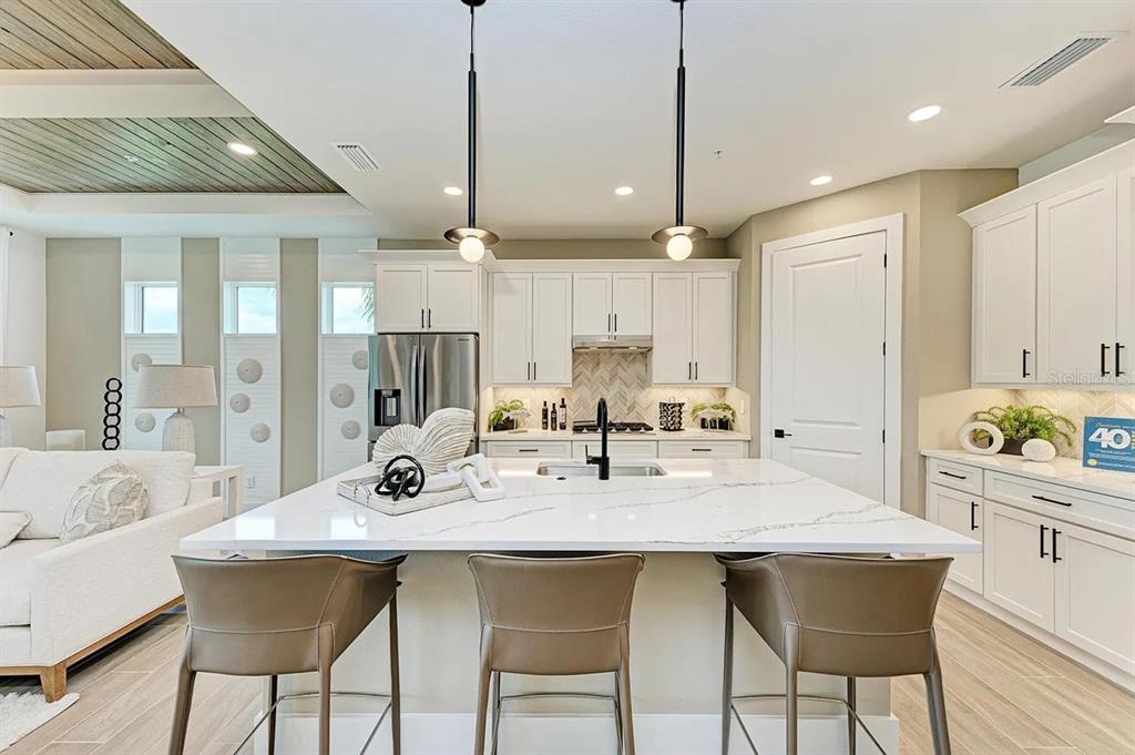 A modern kitchen features white cabinetry, a large marble-topped island, and two pendant lights — 10016 REMBRANDT WAY UNIT 101, BRADENTON, FL