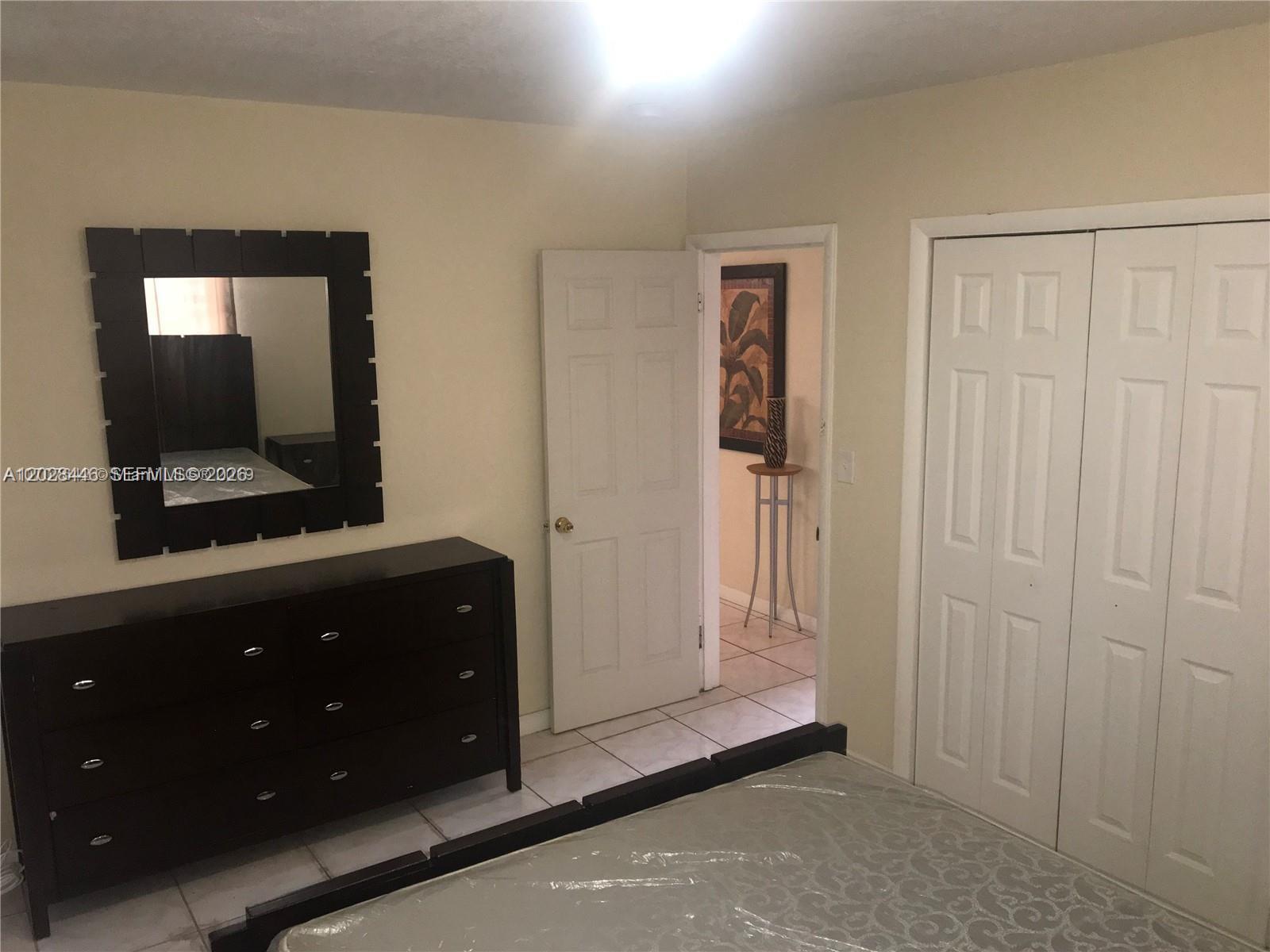 A bedroom features a dark wood dresser, a matching mirror, and white closet doors — 133 NW 57th St # 2, Miami FL 33127, MIAMI, FL