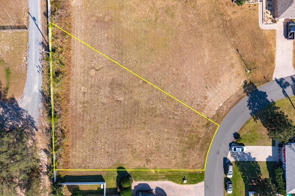 An aerial view shows a vacant, irregularly shaped residential lot outlined in yellow — 1004 MYRTLE BREEZES COURT, FRUITLAND PARK, FL