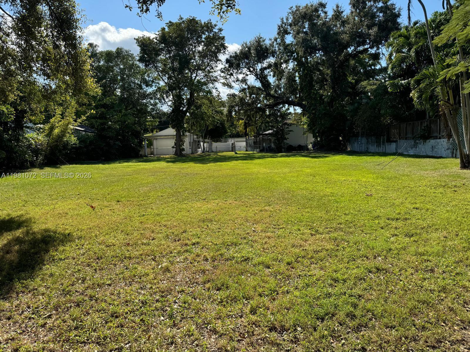 A large, flat, grassy vacant lot is surrounded by mature trees and neighboring residential structures — 3528 Royal Palm Ave, Miami FL 33133, MIAMI, FL