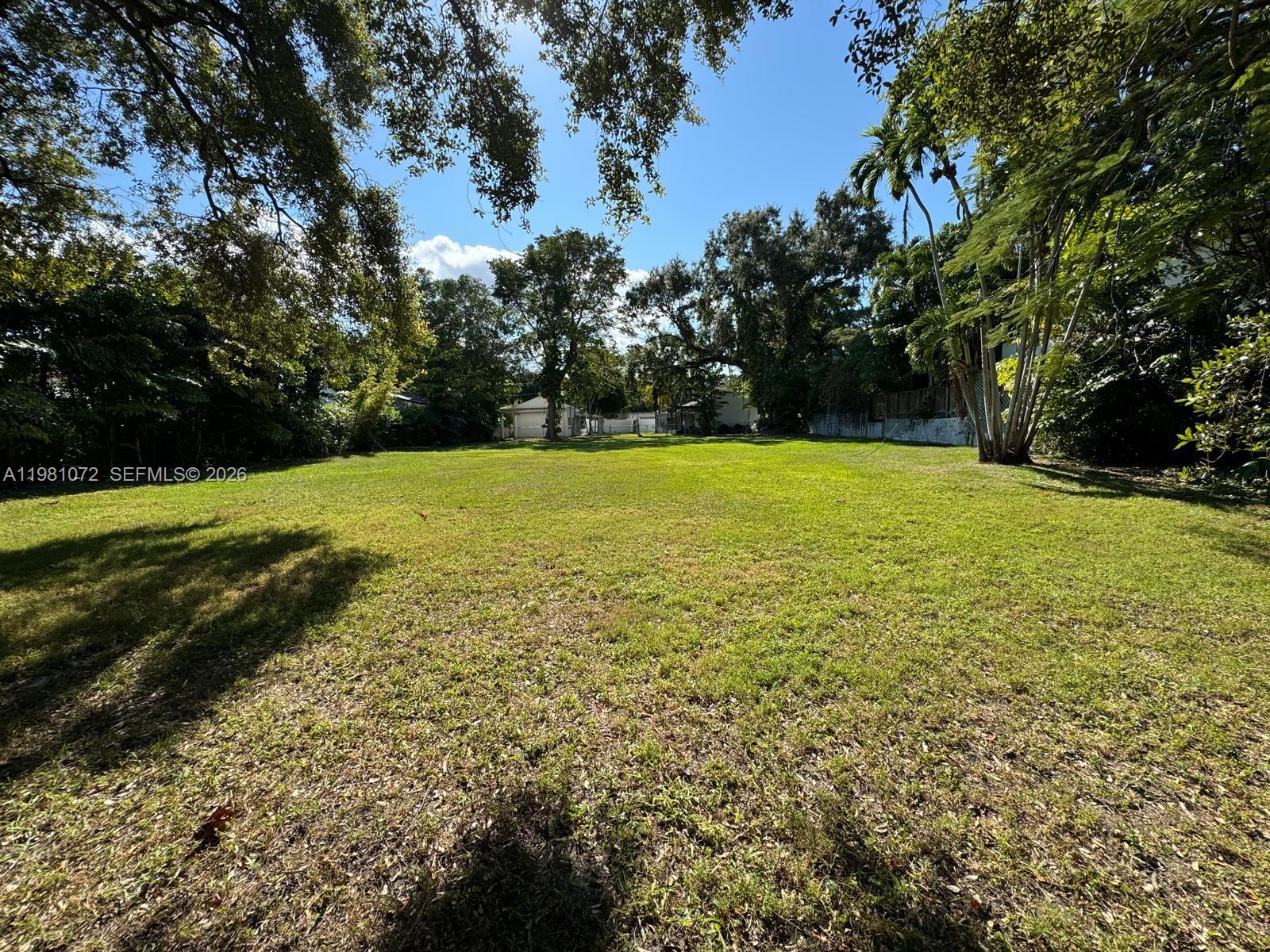 A large, flat, grassy residential lot surrounded by mature trees under a clear blue sky — 3528 Royal Palm Ave, Miami FL 33133, MIAMI, FL