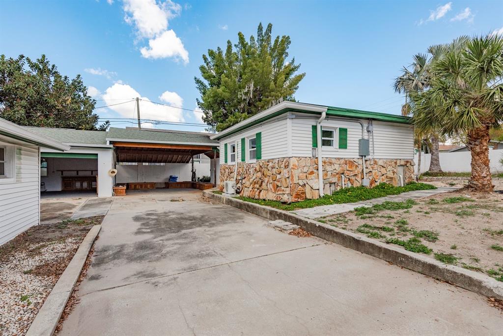 A concrete driveway leads to a carport and a house with stone and white siding — 1115 PENNSYLVANIA AVENUE, PALM HARBOR, FL