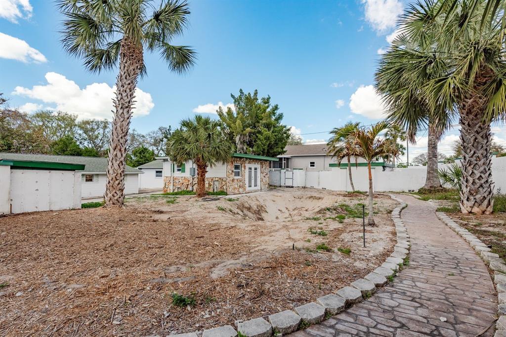 A backyard features a stone-paved path, palm trees, and a small building with stone siding — 1115 PENNSYLVANIA AVENUE, PALM HARBOR, FL