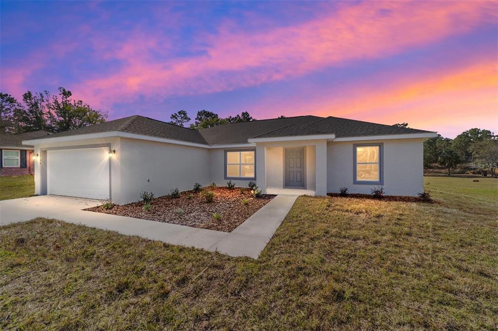A single-story house with a white exterior, a two-car garage, and a landscaped front yard — 6411 SW 204 AVENUE, DUNNELLON, FL