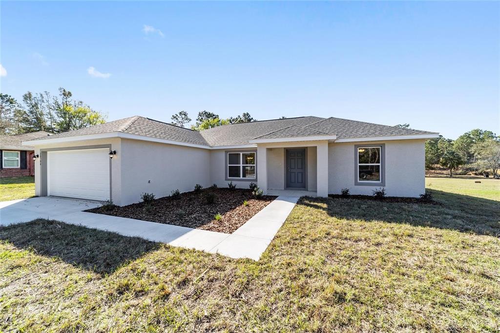 A single-story house with a light-colored stucco exterior, a two-car garage, and a front walkway — 6411 SW 204 AVENUE, DUNNELLON, FL