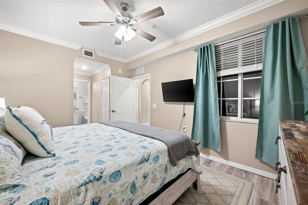 A bedroom features a queen bed, a ceiling fan, a wall-mounted television, and teal curtains — 43020 GREENWAY BOULEVARD UNIT 312, PUNTA GORDA, FL